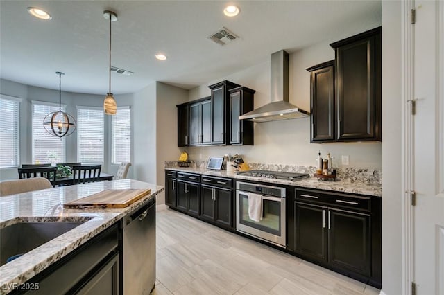 7194 Sage Wren Ct, Las Vegas, NV 89148 - kitchen with appliances with stainless steel finishes, wall chimney exhaust hood, a chandelier, recessed lighting, and light stone countertops