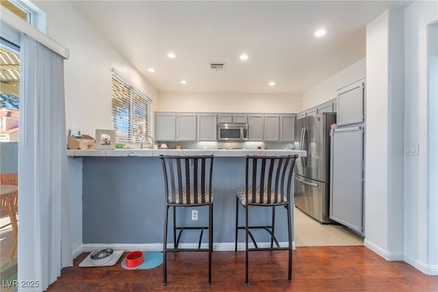 2789 Trotwood Ln, Las Vegas, NV 89108 - kitchen with stainless steel appliances, gray cabinets, a peninsula, a kitchen bar, and recessed lighting