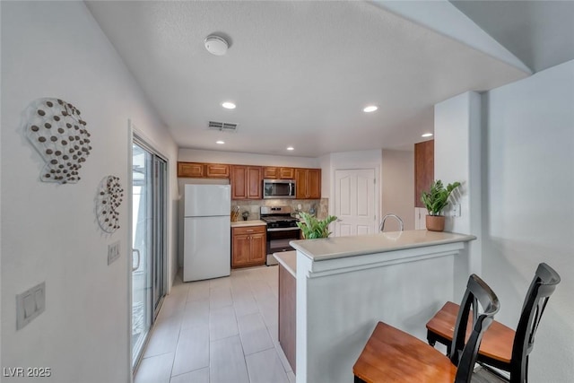 8567 Little Fox St, Las Vegas, NV 89123 - kitchen with appliances with stainless steel finishes, brown cabinetry, a peninsula, light countertops, and tasteful backsplash