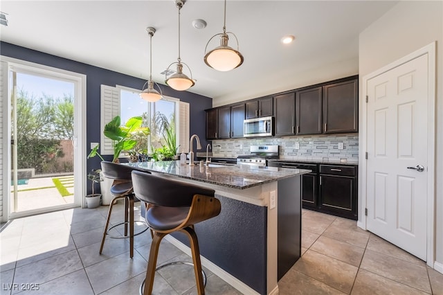 7732 Bandon Cliffs St, North Las Vegas, NV 89084 - kitchen with stainless steel appliances, dark stone counters, tasteful backsplash, a center island with sink, and a breakfast bar area