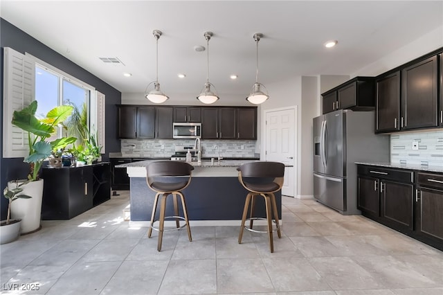 7732 Bandon Cliffs St, North Las Vegas, NV 89084 - kitchen with stainless steel appliances, tasteful backsplash, light stone counters, a kitchen bar, and hanging light fixtures