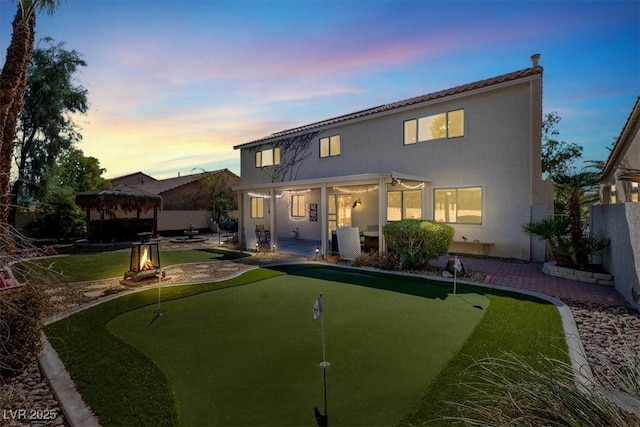 1306 Big Tree Ave, North Las Vegas, NV 89031 - back of house at dusk with an area to practice putting, a patio, a gazebo, stucco siding, and a fire pit