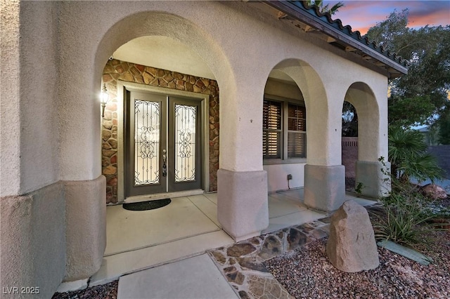 9008 Sawhill Pond St, Las Vegas, NV 89131 - exterior entry at dusk featuring stucco siding, french doors, stone siding, and covered porch