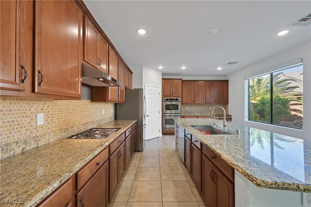 9008 Sawhill Pond St, Las Vegas, NV 89131 - kitchen with under cabinet range hood, a sink, appliances with stainless steel finishes, tasteful backsplash, and brown cabinets