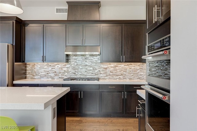 11280 Granite Ridge Dr Unit 1009, Las Vegas, NV 89135 - kitchen featuring under cabinet range hood, stainless steel appliances, dark brown cabinets, and tasteful backsplash