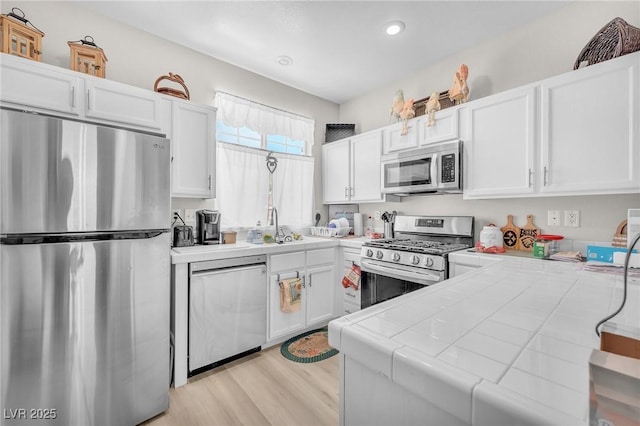 1011 Dancing Vines Ave, Las Vegas, NV 89183 - kitchen with appliances with stainless steel finishes, tile countertops, white cabinets, light wood-style floors, and recessed lighting