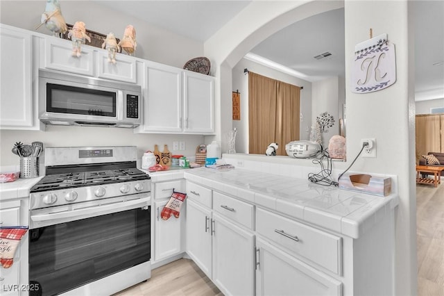 1011 Dancing Vines Ave, Las Vegas, NV 89183 - kitchen with stainless steel appliances, arched walkways, white cabinets, and light wood finished floors