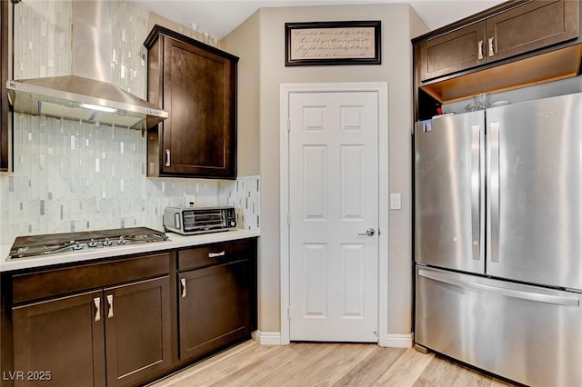 1425 Overseer Ave, Henderson, NV 89074 - kitchen with appliances with stainless steel finishes, wall chimney range hood, dark brown cabinets, light wood-type flooring, and tasteful backsplash
