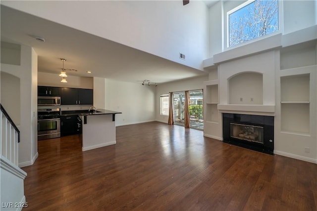 5256 Harvest Breeze Rd, Las Vegas, NV 89118 - unfurnished living room with dark wood finished floors, a towering ceiling, a tile fireplace, baseboards, and built in features