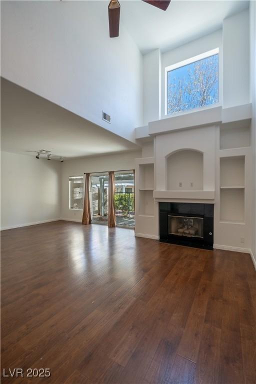 5256 Harvest Breeze Rd, Las Vegas, NV 89118 - unfurnished living room featuring dark wood-style flooring, a glass covered fireplace, built in shelves, a high ceiling, and baseboards
