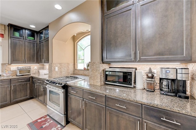9729 Hawk Crest St, Las Vegas, NV 89141 - kitchen with stainless steel appliances, light stone countertops, dark brown cabinetry, arched walkways, and recessed lighting