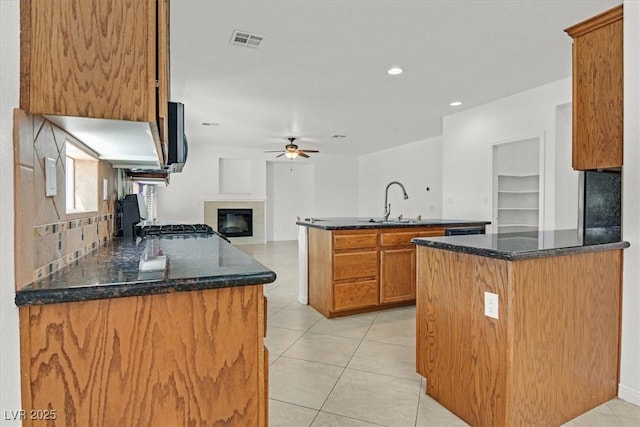3689 Bufflehead St, Las Vegas, NV 89122 - kitchen with ceiling fan, a sink, a glass covered fireplace, dark stone counters, and a kitchen island with sink