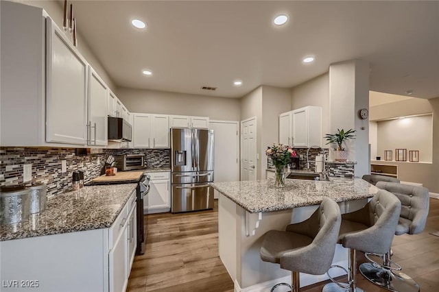 672 Solitude Point Ave, Henderson, NV 89012 - kitchen featuring appliances with stainless steel finishes, light stone counters, a breakfast bar area, decorative backsplash, and light wood finished floors