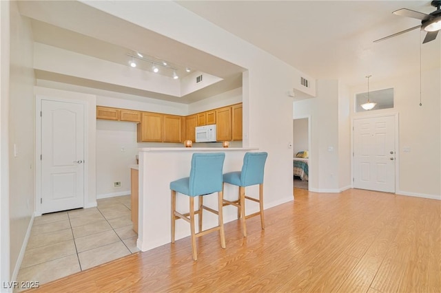 8985 S Durango Dr Unit 1177, Las Vegas, NV 89113 - kitchen featuring white microwave, ceiling fan, a tray ceiling, a peninsula, and brown cabinetry