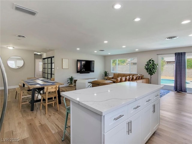 4072 E Harmon Ave, Las Vegas, NV 89121 - kitchen featuring a kitchen island, recessed lighting, white cabinets, light wood finished floors, and light stone counters