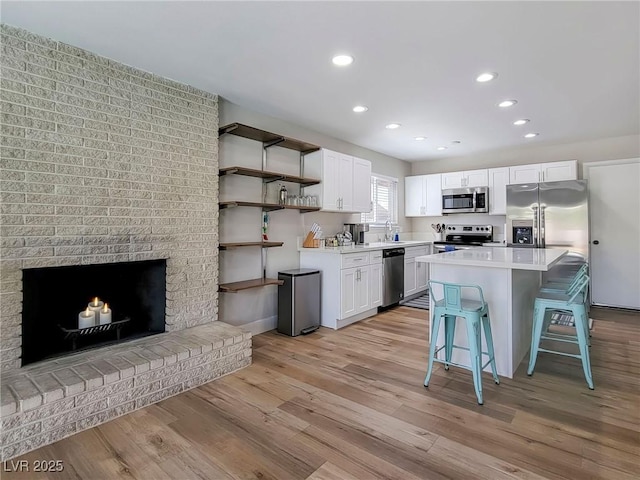 4072 E Harmon Ave, Las Vegas, NV 89121 - kitchen with stainless steel appliances, a breakfast bar area, open shelves, white cabinetry, and light wood-type flooring