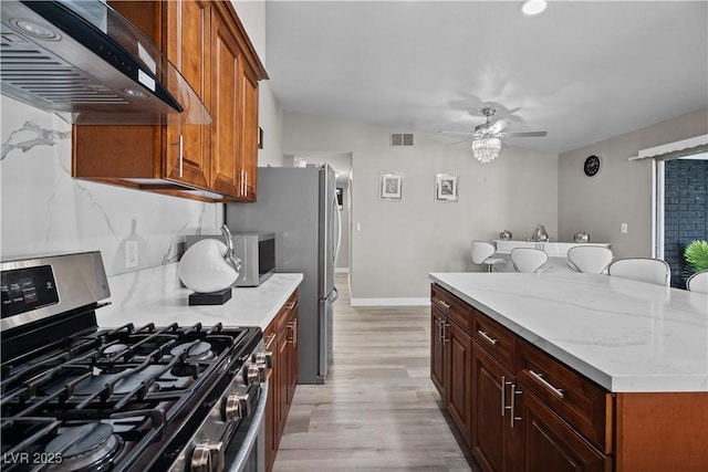 5375 Chestnut St, Las Vegas, NV 89119 - kitchen featuring stainless steel appliances, wall chimney range hood, ceiling fan, light wood-type flooring, and light stone countertops