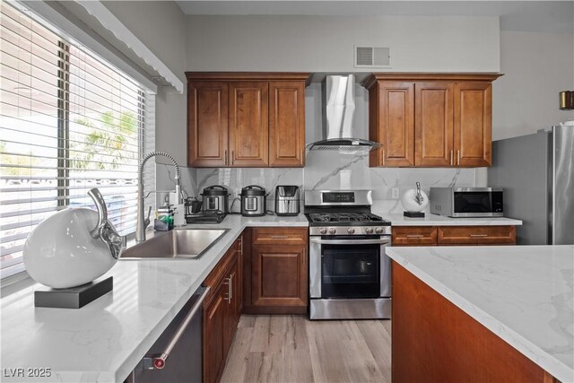 5375 Chestnut St, Las Vegas, NV 89119 - kitchen with wall chimney range hood, stainless steel appliances, light wood-type flooring, brown cabinets, and light stone counters