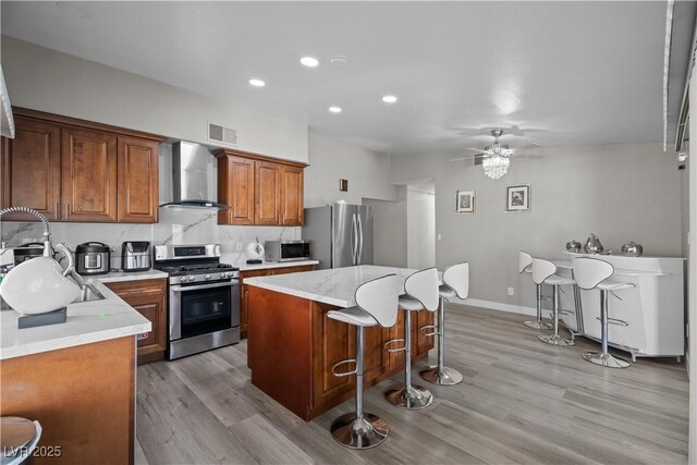 5375 Chestnut St, Las Vegas, NV 89119 - kitchen with wall chimney exhaust hood, stainless steel appliances, light wood-type flooring, a kitchen island, and ceiling fan