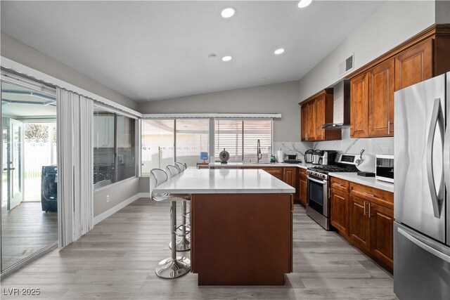 5375 Chestnut St, Las Vegas, NV 89119 - kitchen featuring appliances with stainless steel finishes, wall chimney exhaust hood, a kitchen breakfast bar, vaulted ceiling, and a center island