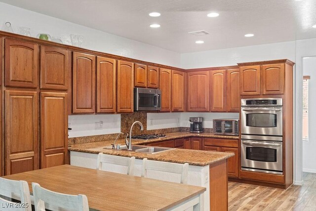 7252 Royal Melbourne Dr, Las Vegas, NV 89131 - kitchen with stainless steel appliances, a sink, a peninsula, light wood-type flooring, and brown cabinets