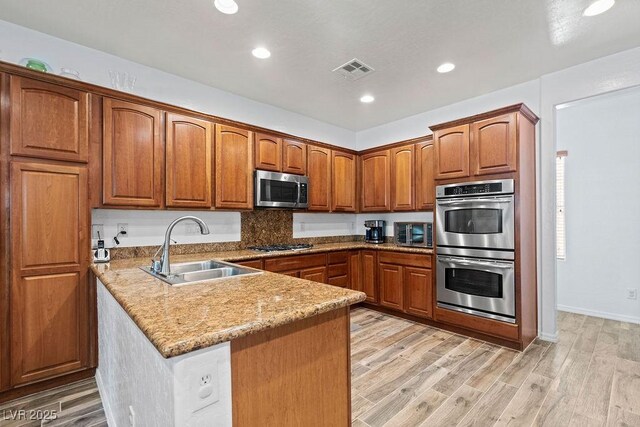 7252 Royal Melbourne Dr, Las Vegas, NV 89131 - kitchen with appliances with stainless steel finishes, a sink, a peninsula, brown cabinetry, and light wood-style flooring