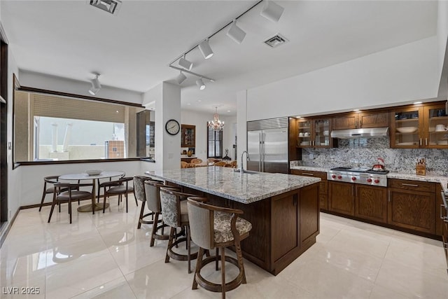 2925 Coast Line Ct, Las Vegas, NV 89117 - kitchen featuring stainless steel appliances, under cabinet range hood, backsplash, light stone countertops, and glass insert cabinets