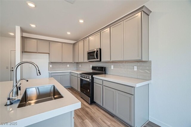 9842 Lost Horse Ave, Las Vegas, NV 89178 - kitchen with stainless steel appliances, a sink, gray cabinetry, light wood-type flooring, and backsplash
