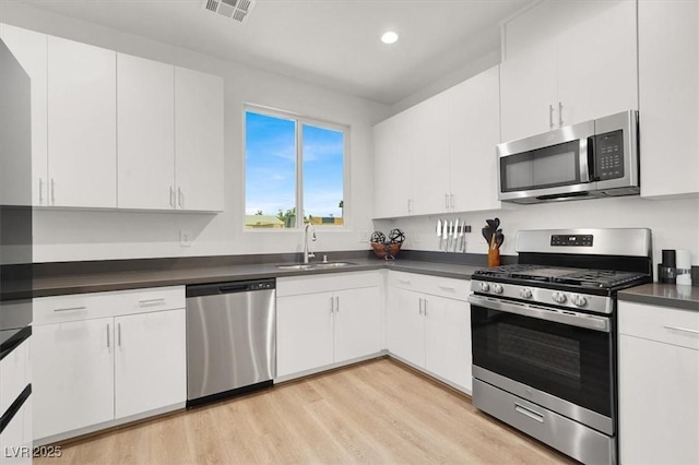 66 Chelsea Manor Ct, Las Vegas, NV 89110 - kitchen featuring stainless steel appliances, a sink, dark countertops, light wood-style floors, and white cabinetry