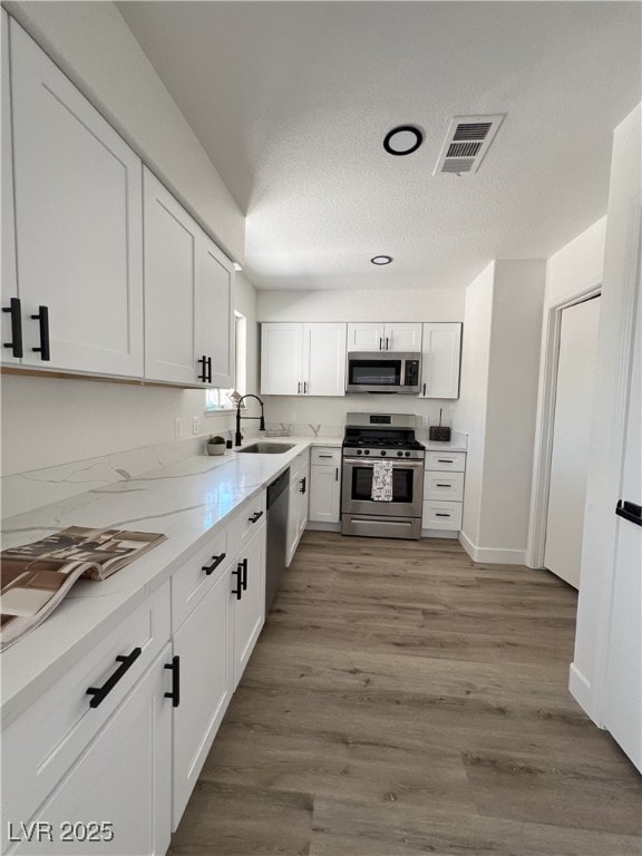 8068 Cetus Cir, Las Vegas, NV 89128 - kitchen featuring stainless steel appliances, a sink, white cabinetry, wood finished floors, and a textured ceiling