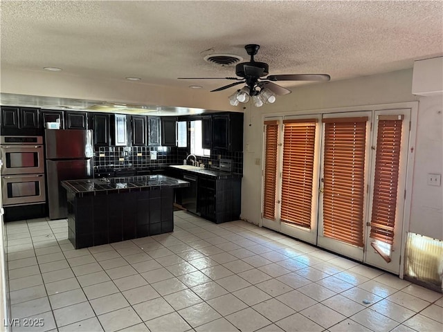 1674 Seneca Ln, Las Vegas, NV 89169 - kitchen with dark cabinetry, stainless steel appliances, light tile patterned flooring, and a textured ceiling