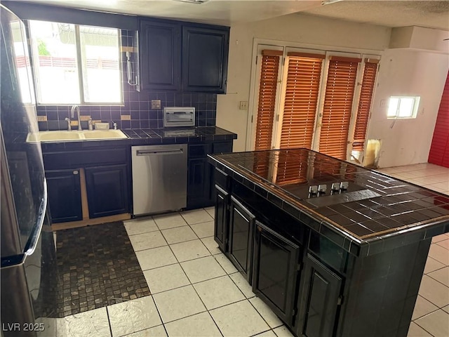 1674 Seneca Ln, Las Vegas, NV 89169 - kitchen with tile counters, stainless steel dishwasher, a sink, tasteful backsplash, and freestanding refrigerator