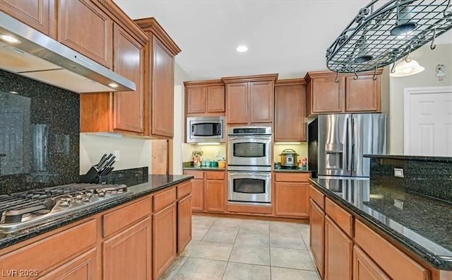 10001 Blairwood Ct, Las Vegas, NV 89178 - kitchen featuring appliances with stainless steel finishes, under cabinet range hood, light tile patterned flooring, dark stone countertops, and tasteful backsplash