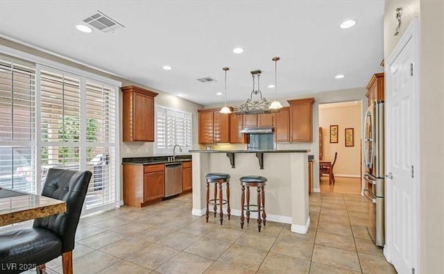 10001 Blairwood Ct, Las Vegas, NV 89178 - kitchen with appliances with stainless steel finishes, a kitchen breakfast bar, brown cabinetry, a kitchen island, and recessed lighting