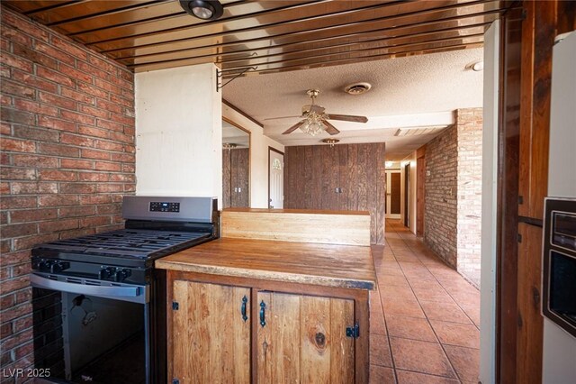 4516 E Flamingo Rd, Las Vegas, NV 89121 - kitchen with brick wall, stainless steel gas range oven, ceiling fan, and light tile patterned floors