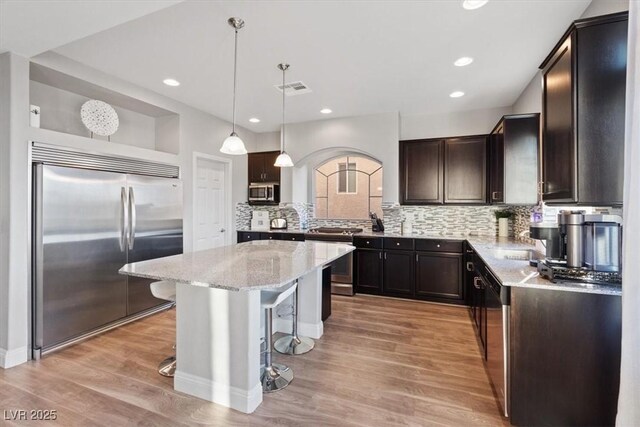 6056 Atlantis Dream Ave, Las Vegas, NV 89139 - kitchen featuring appliances with stainless steel finishes, a breakfast bar, light stone counters, light wood-style floors, and a center island