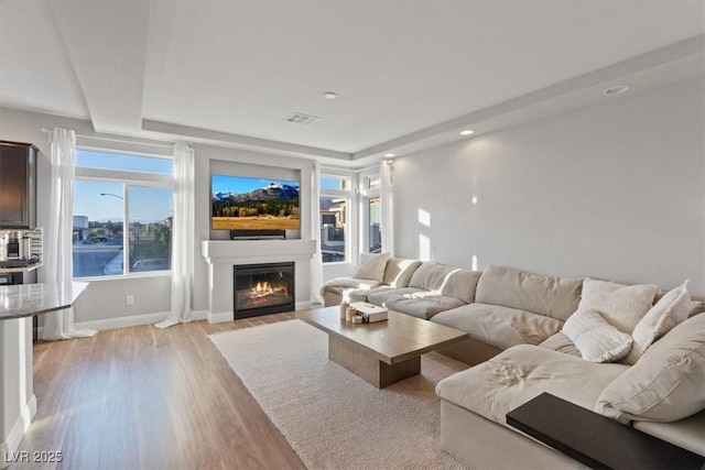 6056 Atlantis Dream Ave, Las Vegas, NV 89139 - living area featuring light wood-style flooring, a raised ceiling, a glass covered fireplace, plenty of natural light, and recessed lighting