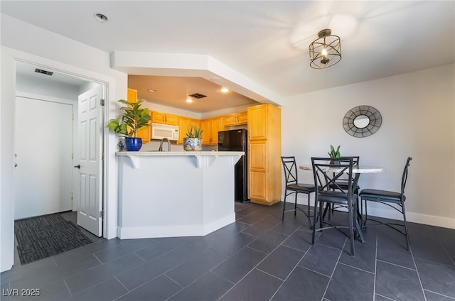 7288 Quarterhorse Ln, Las Vegas, NV 89148 - kitchen featuring white microwave, freestanding refrigerator, a peninsula, light countertops, and a breakfast bar area