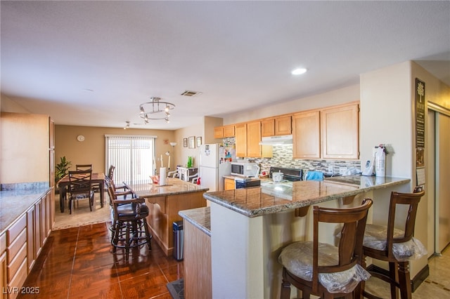 7801 Olympus Ave, Las Vegas, NV 89131 - kitchen with white appliances, under cabinet range hood, decorative backsplash, a kitchen island, and light brown cabinets