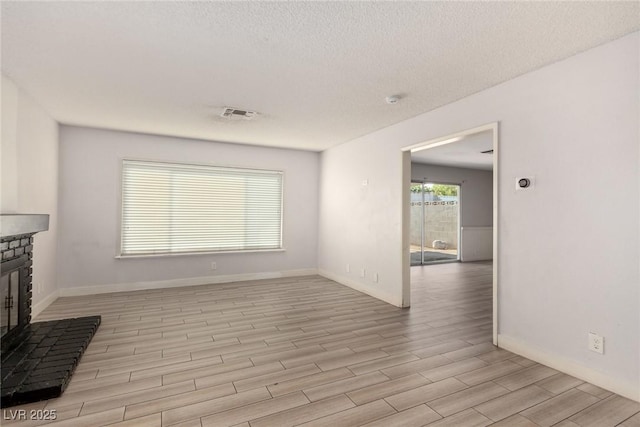 1704 Kismet Cir, Las Vegas, NV 89108 - unfurnished living room with light wood finished floors, a glass covered fireplace, a textured ceiling, and baseboards