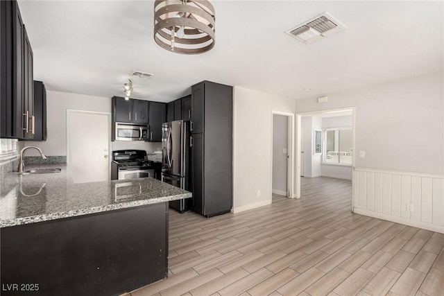 1704 Kismet Cir, Las Vegas, NV 89108 - kitchen featuring appliances with stainless steel finishes, a sink, light stone countertops, light wood finished floors, and wainscoting