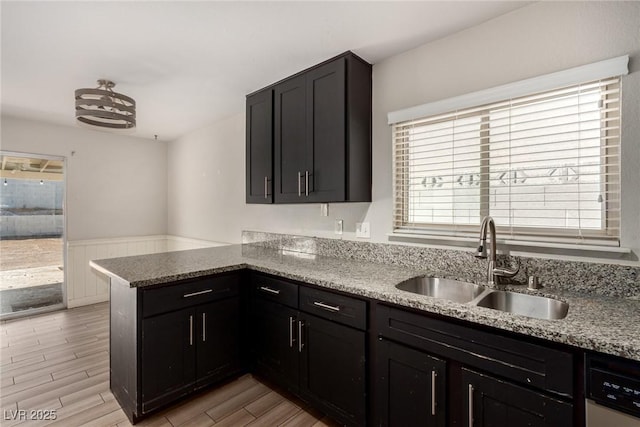 1704 Kismet Cir, Las Vegas, NV 89108 - kitchen featuring a sink, a peninsula, light stone counters, light wood-style flooring, and wainscoting