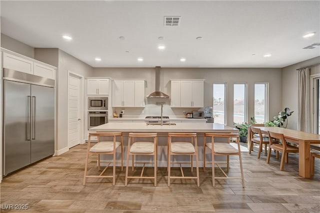 7736 Tioga Ridge Ct, Las Vegas, NV 89117 - kitchen featuring built in appliances, wall chimney range hood, recessed lighting, a center island with sink, and light countertops