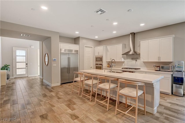 7736 Tioga Ridge Ct, Las Vegas, NV 89117 - kitchen featuring built in appliances, wall chimney range hood, recessed lighting, light wood finished floors, and a breakfast bar
