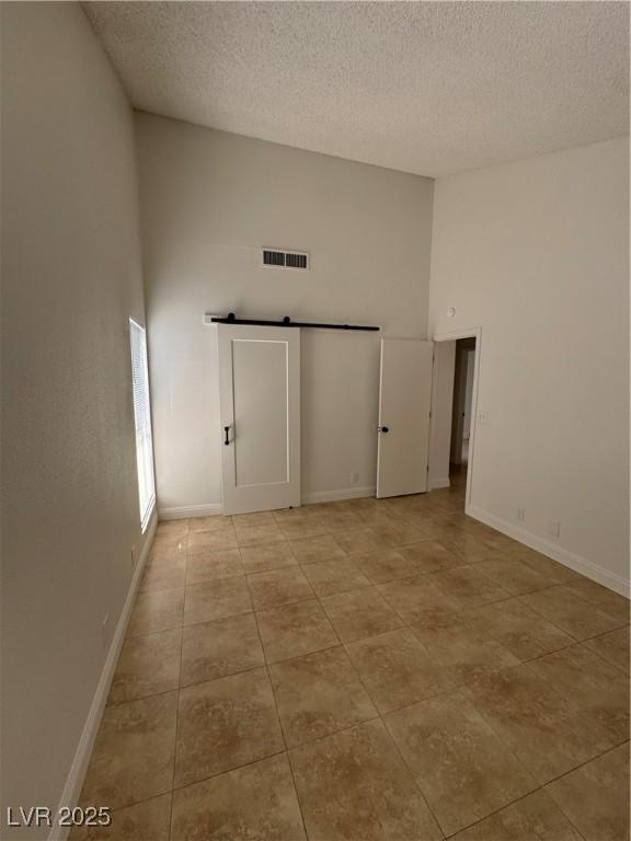2318 El Molino Cir, Las Vegas, NV 89108 - empty room featuring a high ceiling, a textured ceiling, light tile patterned floors, and a barn door