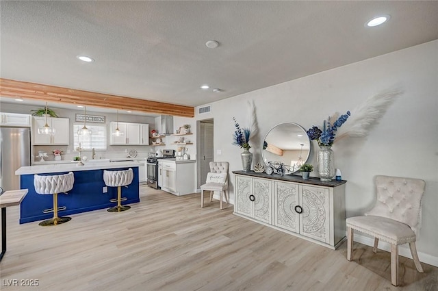 700 Cactus Ln, Las Vegas, NV 89107 - kitchen featuring appliances with stainless steel finishes, light wood-style floors, white cabinetry, a breakfast bar area, and a textured ceiling