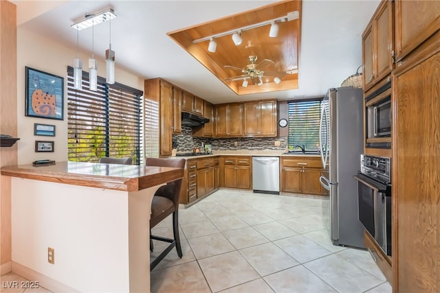 2857 San Lago Ct, Las Vegas, NV 89121 - kitchen with appliances with stainless steel finishes, a tray ceiling, brown cabinetry, track lighting, and a ceiling fan