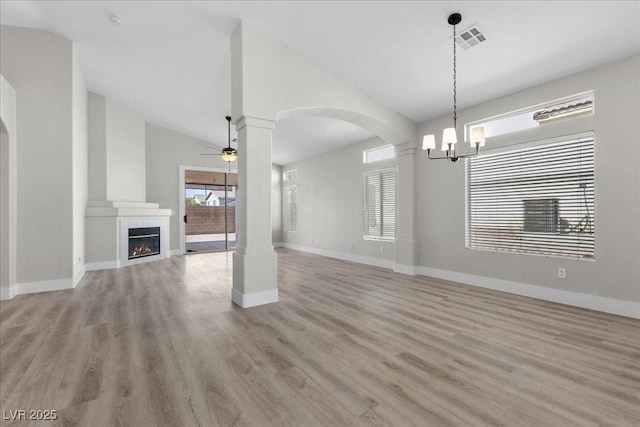10613 Tiffanieville Ct, Las Vegas, NV 89129 - unfurnished living room featuring ceiling fan, vaulted ceiling, light wood-style flooring, a tile fireplace, and arched walkways