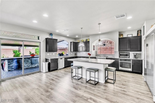 5976 Rockway Glen Ave, Las Vegas, NV 89141 - kitchen with appliances with stainless steel finishes, a kitchen bar, decorative backsplash, a center island, and light wood-style flooring