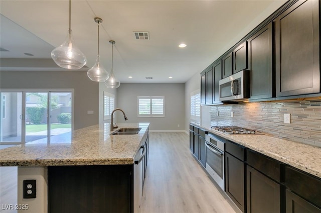 6085 Ryan Ranch Ave, Las Vegas, NV 89130 - kitchen with appliances with stainless steel finishes, light wood-style floors, tasteful backsplash, a center island with sink, and light stone counters